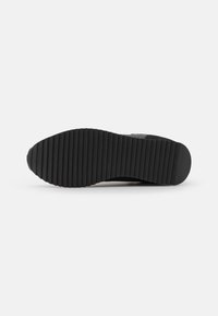 Black sneaker outsole featuring a ribbed, textured surface for traction; durable rubber material, rounded heel, and logo detailing.