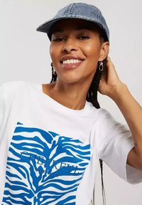 Biała koszulka z niebieskim wzorem w paski zebry i napisem "WESOŁY". W komplecie z dżinsową czapką.