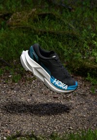 Black athletic shoe with a white sole and teal accents. Features a textured upper, round toe, and bold logo on the side.