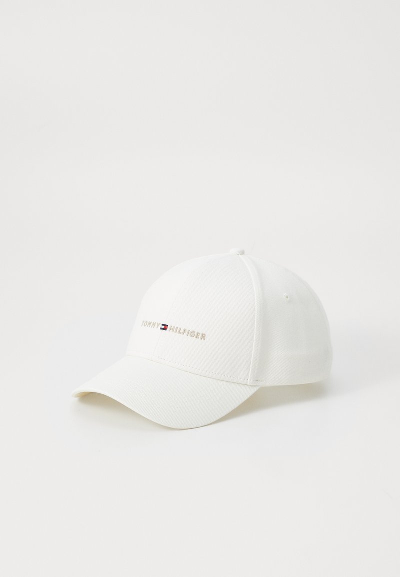 White baseball cap made of cotton twill with a curved brim. Features "TOMMY HILFIGER" logo in gold and red-blue accents on the front.