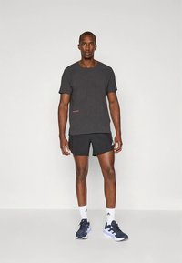 Harmaa lyhythihainen urheilupaita, jossa on hienovarainen kuvio, yhdistettynä mustiin shortseihin ja tummansinisiin juoksukenkiin, joissa on valkoisia yksityiskohtia.