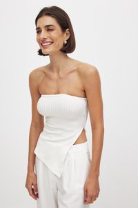Witte strapless top met textuur ribbelstructuur, asymmetrische zoom en zijcut-out. Gecombineerd met hoge taille witte broek.