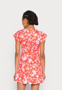 Vestido de manga curta em coral com padrão floral rosa, corpo justo, saia rodada e textura de tecido suave.