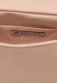 Vaaleanpunainen kangaslaukun sisustus, jossa on sileä pinta, ja jossa on näkyvä etiketti "ANNA FIELD" ommeltuna vuoriin.