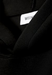 Gros plan d'un tissu de vêtement noir avec une étiquette blanche partiellement visible montrant le mot "WEEK."