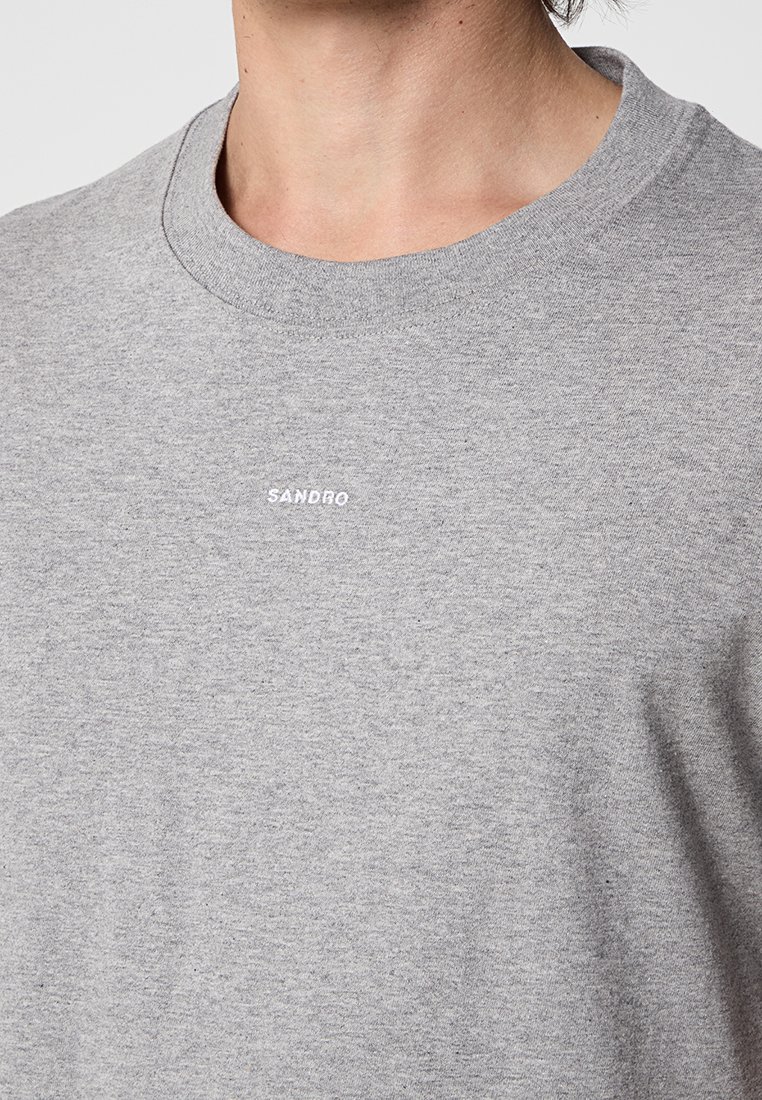 Grijze katoenen t-shirt met een ronde hals, met een klein wit "SANDRO" logo op de borst. Zachte, gestructureerde stof met een relaxte pasvorm.