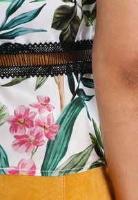 Blusa floreale con sfondo bianco, caratterizzata da foglie verdi e fiori rosa, accentuata da un bordo in pizzo nero e una texture in satin liscia.