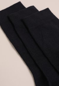 Schwarze Baumwollsocken, die in drei Stapeln angeordnet sind, mit einem gerippten Muster und elastischen Bündchen, auf einem hellen Hintergrund präsentiert.
