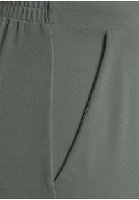 Green fabric pants featuring an elastic waistband with a side pocket. The texture is smooth and the design is simple and functional.