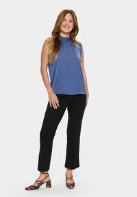 Top blu senza maniche con scollo arricciato, abbinato a pantaloni neri alla caviglia e scarpe con tacco a blocco con stampa leopardata.