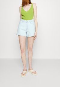 Grön stickad linne, ljusblå denimshorts och off-white plattformssandaler. Shorts har hög midja och klassisk femficksdesign.