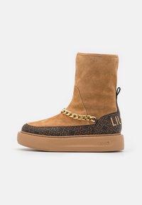 Zamszowy botek za kostkę w kolorze koniakowym z teksturowanym ciemnym wzorem i złotym łańcuszkiem jako akcentem. Posiada gumową podeszwę i detal z logo po boku.