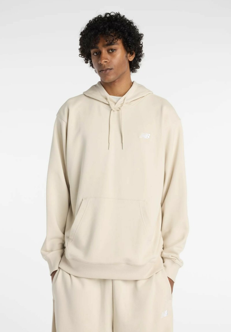 Felpa con cappuccio beige realizzata in tessuto morbido, con tasca frontale e cordino, decorata con un piccolo logo bianco sul petto.