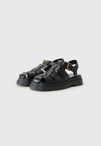Zwarte leren sandalen met meerdere banden, een dikke zool en gouden hardwareaccenten met een verstelbare gesp.