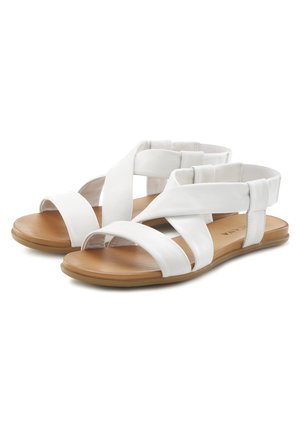 White sandal featuring multiple crossed straps, an open toe, flat sole, and a tan footbed. Material appears smooth with a matte finish.