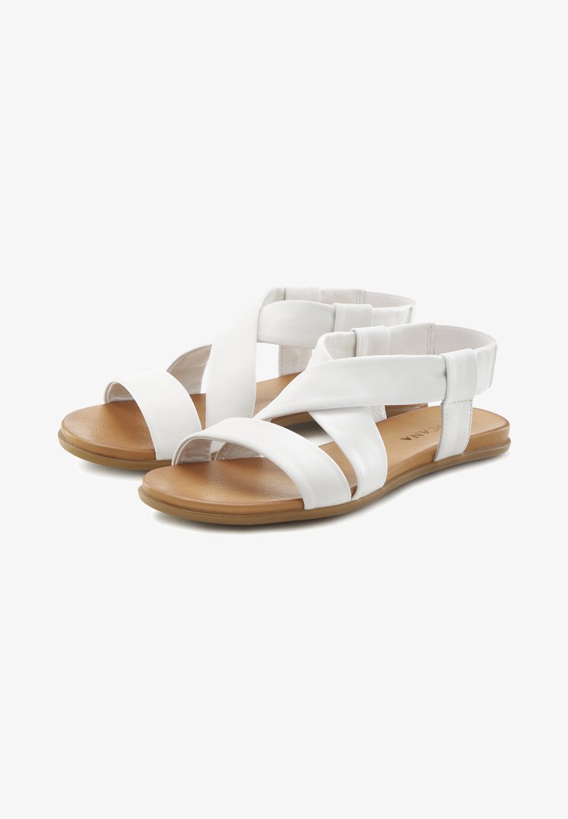 Witte sandaal met meerdere gekruiste banden, een open teen, een platte zool en een tan voetbed. Het materiaal lijkt glad met een matte afwerking.