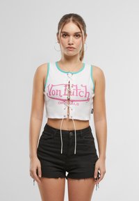 Hvit, kort tanktopp med lyseblå kanter og rosa "Von Dutch"-logo, med en sentral snøring. Kombinert med svarte shorts.