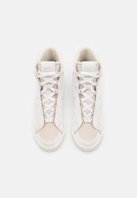 Hvite høye sneakers med en glatt læroverdel, som har myke aksenter i en beige nyanse, snøring og en teksturert gummisåle.