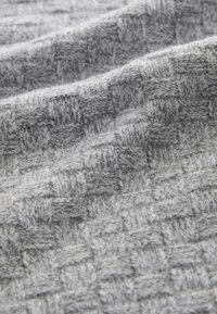 Tessuto lavorato a maglia grigio con motivo a scacchiera testurizzato, caratterizzato da fibre morbide e una superficie leggermente pelosa, che crea profondità e dimensione.