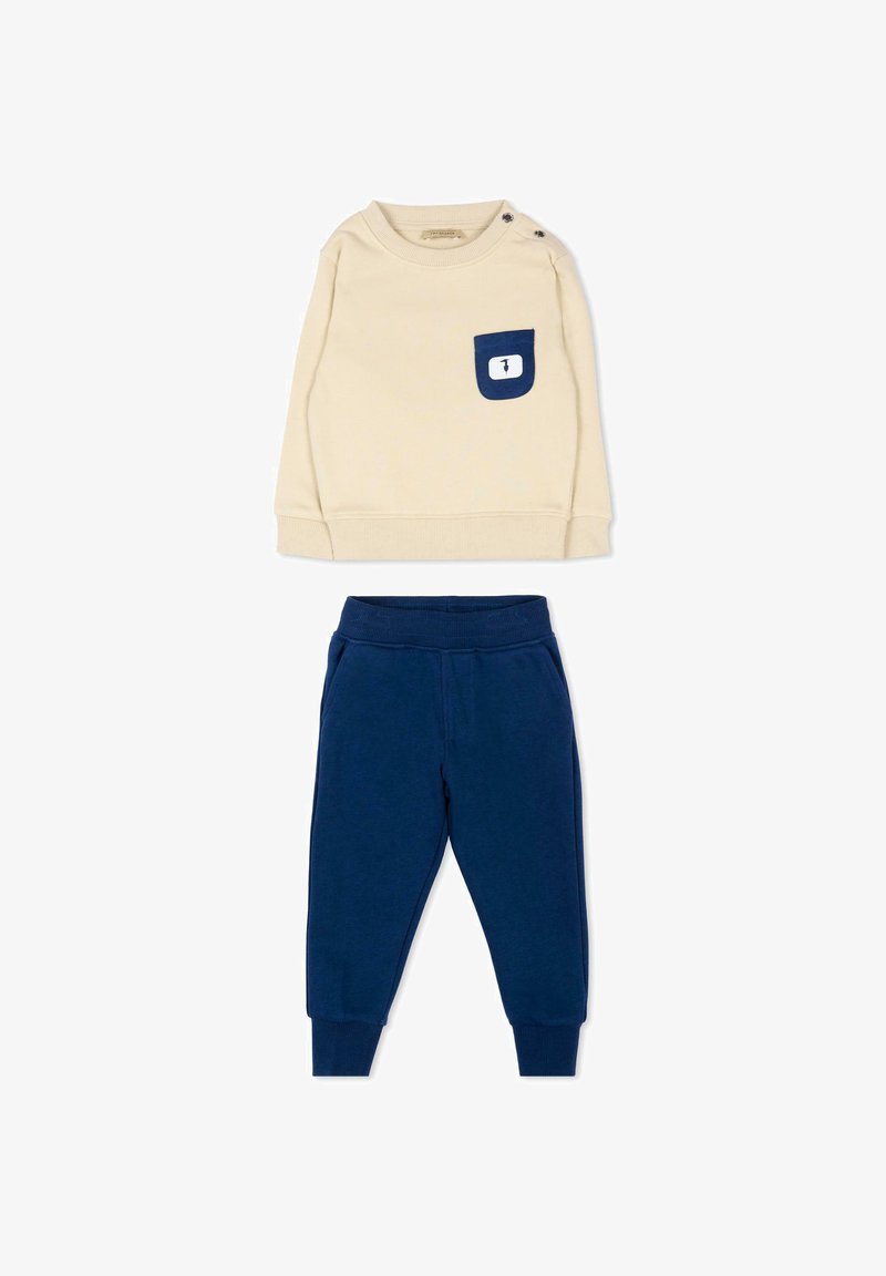 Chemise beige à manches longues avec poche bleu marine et boutons sur l'épaule, associée à un pantalon de jogging bleu marine à taille élastique pour tout-petit.