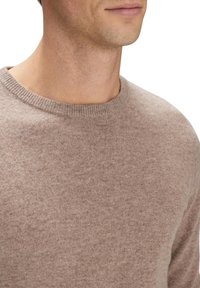 Ljusbrun stickad tröja med rund halsringning. Mjuk textur, kroppsnära passform, minimal detaljering, lämplig för avslappnad användning.