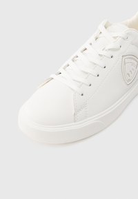 Αθλητικό παπούτσι από λευκό δέρμα με λευκά κορδόνια, υφασμένο πέλμα και γκρι ταμπελάκι με το λογότυπο Blauer στο πλάι, εμφανιζόμενο σε γωνιακή κοντινή λήψη.