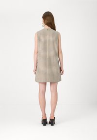 Vestido sem mangas em tons de bege, castanho e azul; apresenta um fecho nas costas e uma forma evasê. Usado com sandálias de salto bloco pretas.