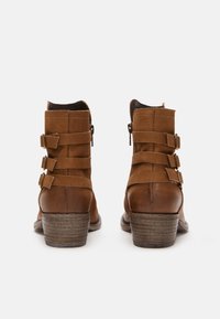 Hnědé kožené kotníkové boty se třemi postranními přezkami a dřevěnými stohovanými podpatky, z pohledu zádního na bílém pozadí.