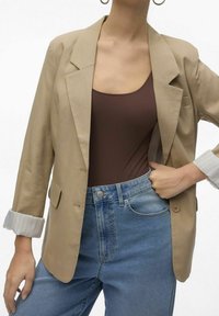 Beige blazer with a structured design, featuring a single pocket and rolled-up striped cuffs, paired with high-waisted blue jeans.