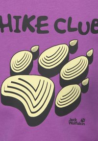 Μωβ ύφασμα με στυλιζαρισμένο κίτρινο και μαύρο αποτύπωμα πατούσας, μερικό κείμενο "HIKE CLUB" και λογότυπο Jack Wolfskin με αποτύπωμα πατούσας.