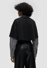 T-shirt nera corta con maniche ampie sopra una lunga maglietta a righe. Presenta un tessuto testurizzato e una vestibilità comoda, abbinata a pantaloni neri eleganti.