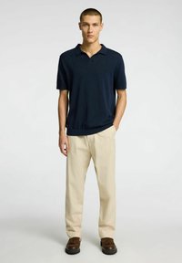 Marinblå pikétröja med korta ärmar, texturerat tyg och V-hals. Kombinerad med ljusbeige byxor och mörkbruna loafers.