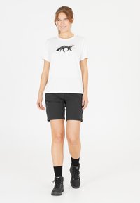 Vit t-shirt med korta ärmar och en svart räv-grafik, parat med svarta shorts med en zip-ficka. Svarta vandringskängor kompletterar outfiten.