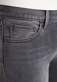 I jeans in denim grigio presentano una texture distintiva con una leggera lucentezza. Sono dotati di una tasca anteriore e di cuciture visibili lungo le cuciture.