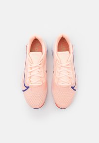 Un paio di scarpe da corsa Nike di colore pesca con logo verde chiaro, suole bianche e accenti blu e rossi, viste dall'alto.
