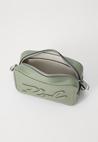 Borsa a mano in pelle verde con finitura texturizzata, chiusura con cerniera e grande logo ricamato sul davanti. L'interno è in tessuto beige.