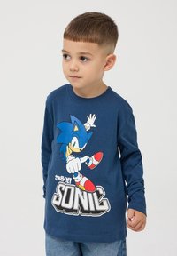 Granatowa koszulka z długim rękawem z nadrukiem postaci z kreskówki w białym kolorze i czerwonymi akcentami. Wykonana z bawełny, z klasycznym okrągłym dekoltem.