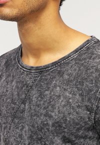 T-shirt nera con texture, colletto rotondo, caratterizzata da un motivo discreto e cuciture a contrasto lungo le cuciture.
