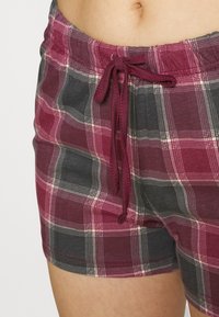 Plaid shorts in shades of burgundy and gray, featuring an elastic waistband with a drawstring and subtle white stitching accents.