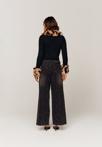 Maglione nero a costine con colletto e polsini in peli sintetici a fantasia, abbinato a jeans neri a gamba larga con applicazioni di borchie argentate.