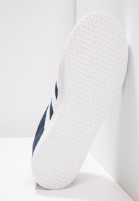 Valge kummikonts sneakeril, millel on tekstuuriga haardemuster. Ülaserv on tumesinine kangas, millel on valged aktsendid ja diagonaalsed triibud külje peal.