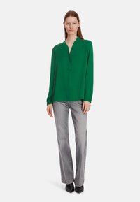 Green long-sleeve blouse with a v-neck and gathered cuffs, paired with grey straight-leg jeans and black pointed-toe heels.