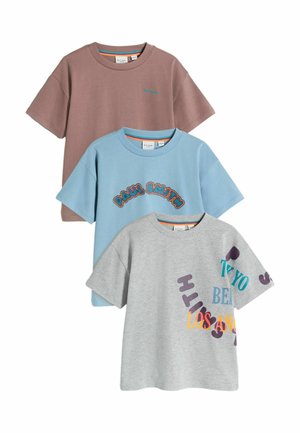 Three T-shirts laid out: one brown, one blue with text, one gray with colorful letters. Each features short sleeves and a relaxed fit.