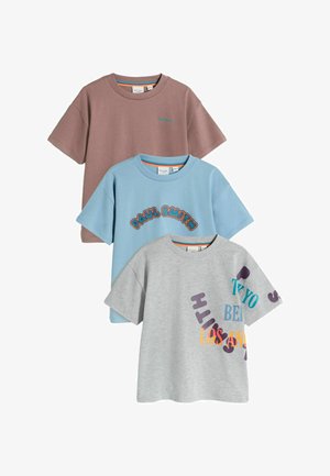 Three T-shirts laid out: one brown, one blue with text, one gray with colorful letters. Each features short sleeves and a relaxed fit.
