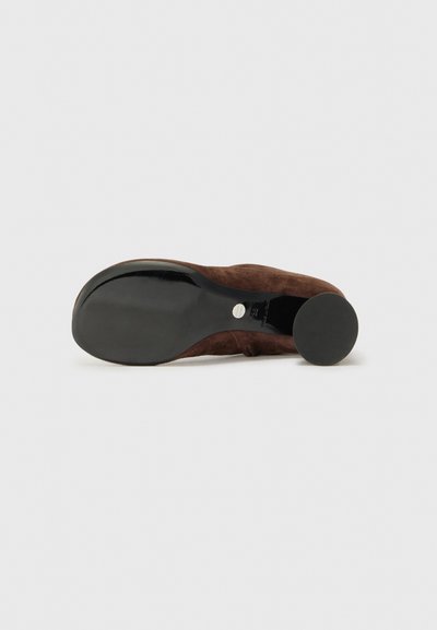 Zapato de ante marrón con suela negra lisa y tacón circular. El diseño presenta una silueta simple y elegante sin adornos.