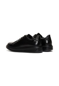 Para czarnych skórzanych niskich sneakersów z grubymi podeszwami, pokazanych z boku i z tyłu na białym tle.