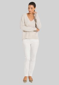 Hellbeige V-Ausschnitt-Pullover aus weichem Strick, kombiniert mit enganliegenden weißen Hosen und gemusterten spitzen Ballerinas. Einfaches und sauberes Design.