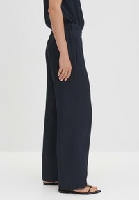 Marineblauwe wijde broek met een elastische tailleband, voorzien van een zachte textuur en zijzakken, gecombineerd met minimalistische zwarte sandalen.