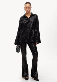 Chemise noire en sequins avec col, associée à un pantalon noir en sequins évasé. Texture lisse, fini brillant et coupe ajustée mettent en valeur la tenue.