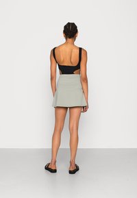 Bodysuit preto sem costas combinado com uma mini saia rodada cinza claro, apresentando uma textura suave e um design simples. Calçado preto completa o visual.